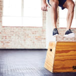 Low section of fit male athlete box jumping in gym