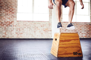Low section of fit male athlete box jumping in gym