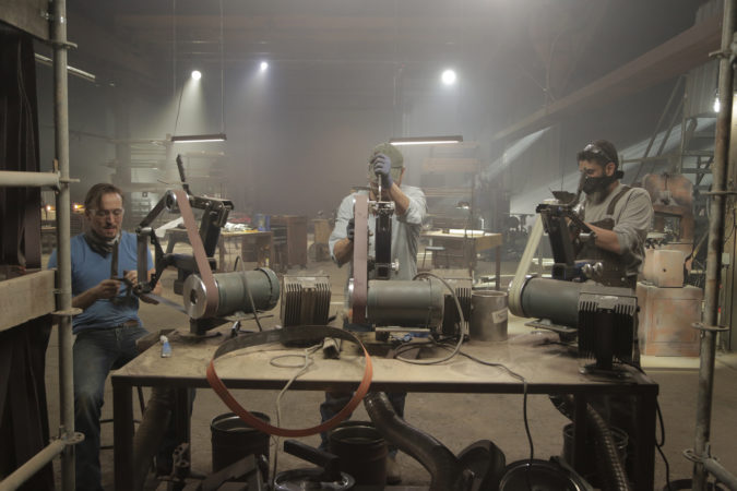 Jason, Luke, and Andreas sand down their weapons in the armory.